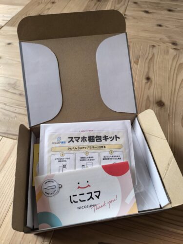 にこスマから届いた中古Pixel 8aのダンボール箱を開封した様子。丁寧な梱包に加え、SIMピン付きのサンキューカードや、古い端末をかんたんに売れる『スマホ梱包キット』が同梱されている実物の写真