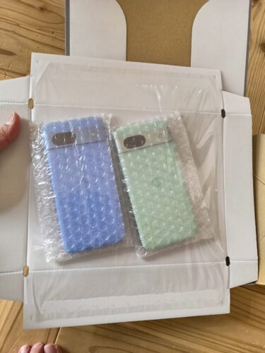 にこスマで購入した中古のGoogle Pixel 8a（夫婦用のブルーとグリーン2台）。本体がそれぞれプチプチで包まれ、さらに透明なフィルムで段ボール板にピタッと強力に固定されており、配送中の衝撃や破損対策が徹底された安心の梱包状態の写真