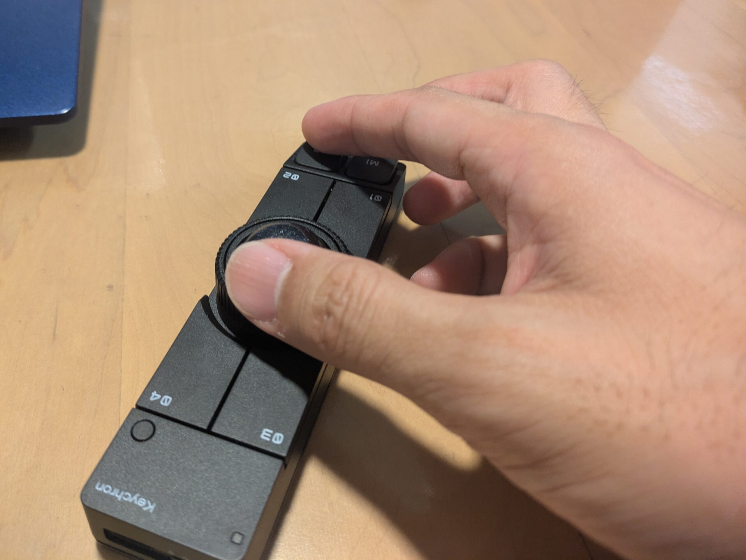 Keychron Nape Proのトラックボールを親指で操作している写真。細長い黒い本体の中央にあるトラックボールと周囲のボタンを手で触り、実際の操作感や指の置き方を確認している。